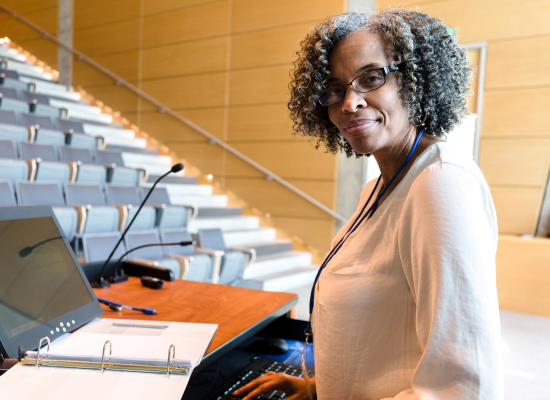 Professor smiling and standing at a podium in a lecture hall