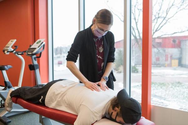 Dr. Kate Henderson, female chiropractor providing a back adjustment and assessment on a male hockey player who is laying face down on the the table at the University of Guelph Health and Performance Centre (HPC)