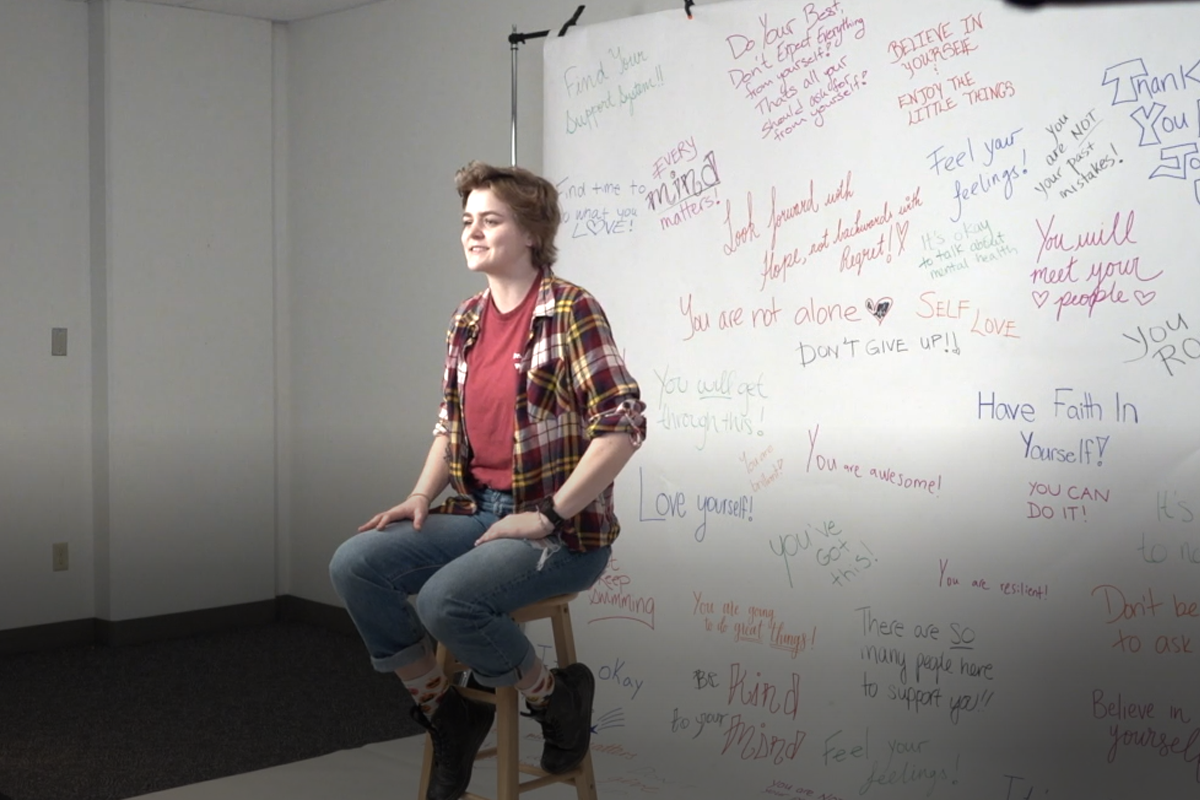 Paige sitting on a stool in front of a white backdrop with positive affirmations written on it
