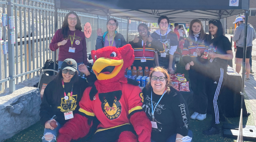 Students posing for photo at Homecoming outreach booth with Gryph macot