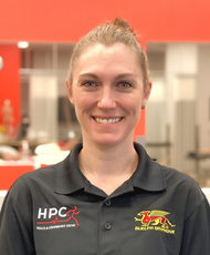 HPC's Dr Kate Henderson, Guelph Chiropractor smiling wearing a black shirt in front of an orange wall