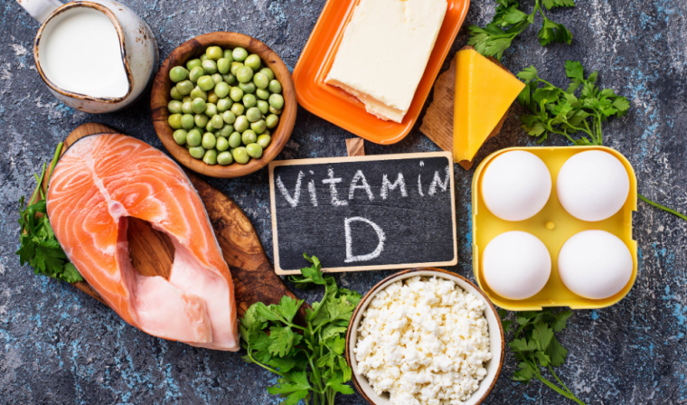 Chalkboard with Vitamin D written on it surrounded by various foods that are rich in vitamin d including salmon, eggs and milk.